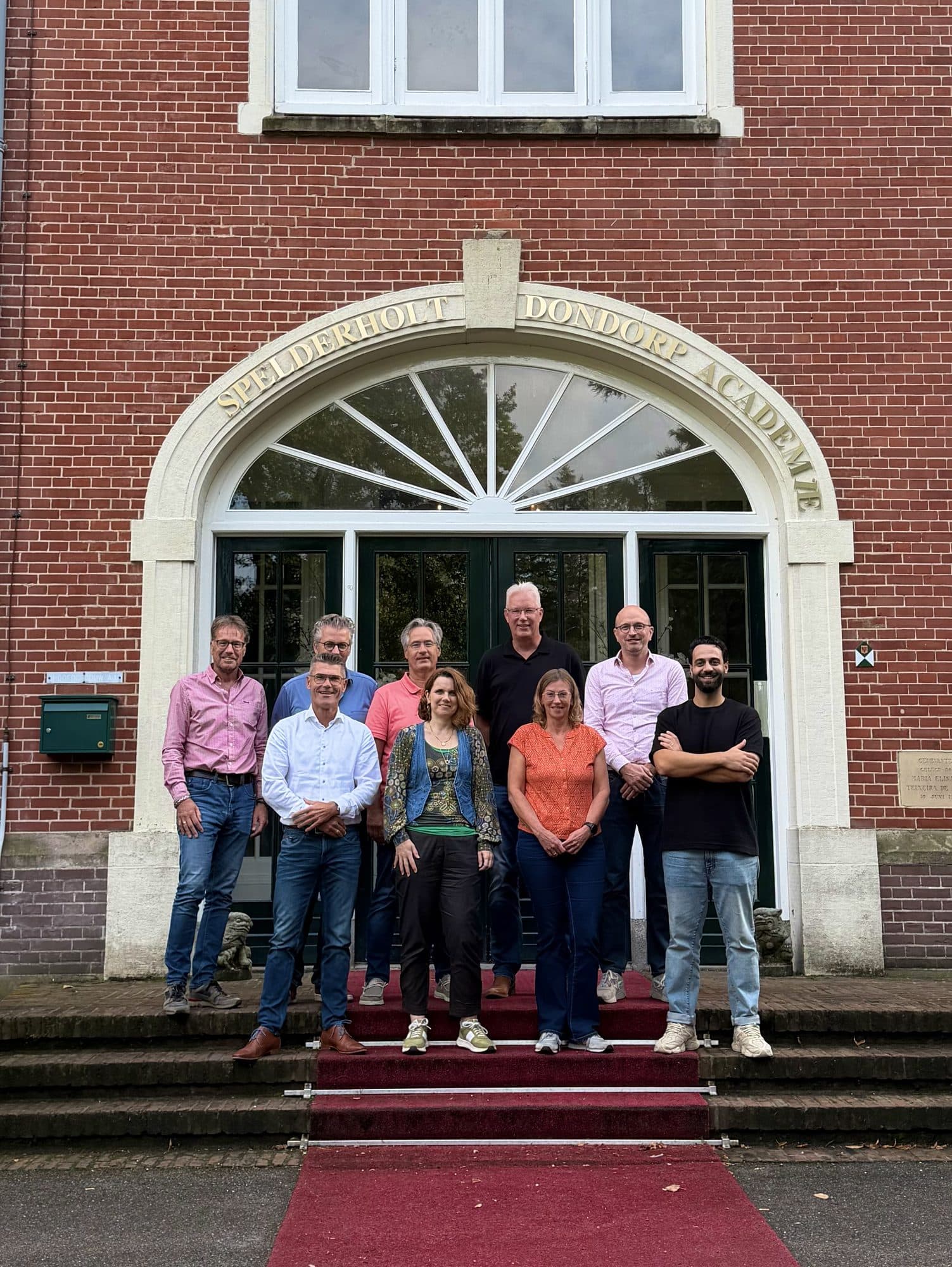 Groep deelnemers op de trappen van een academiegebouw